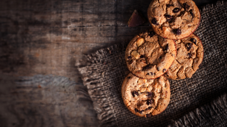 A close-up of keto chocolate chip cookies on a rustic wooden board, with visible chocolate chips and a sprinkle of sea salt—a delicious low-carb dessert and gluten-free treat.