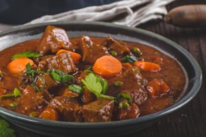 keto beef stew , featuring tender beef chunks simmered in a rich, flavorful broth with keto-friendly vegetables like carrots, celery, and onions. The dish is garnished with fresh herbs and served hot, creating an inviting and appetizing presentation.